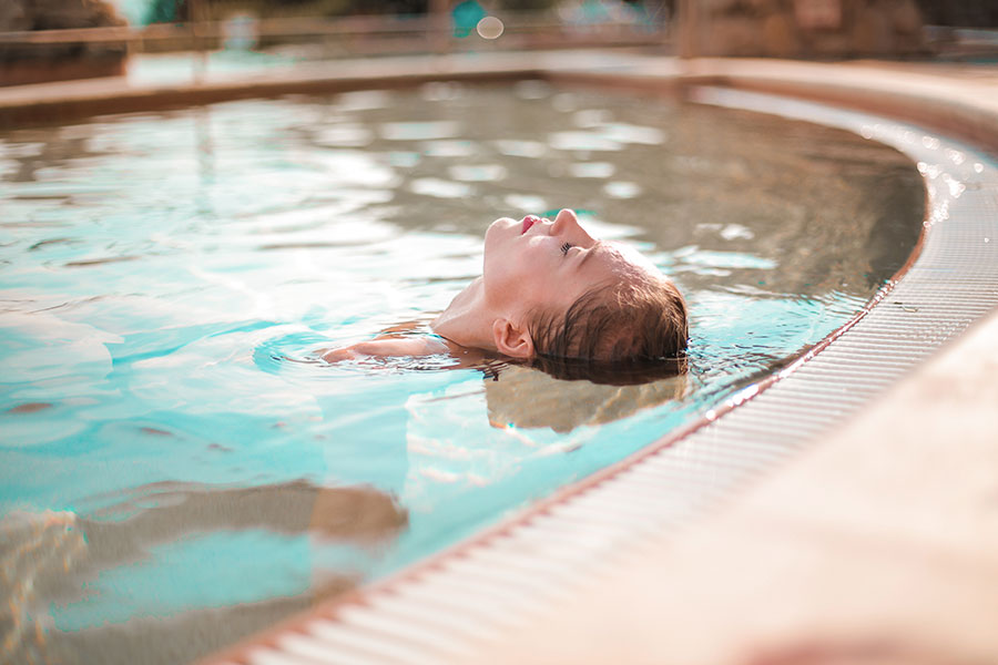 A woman floats on her back submerged up to her neck in a pool.