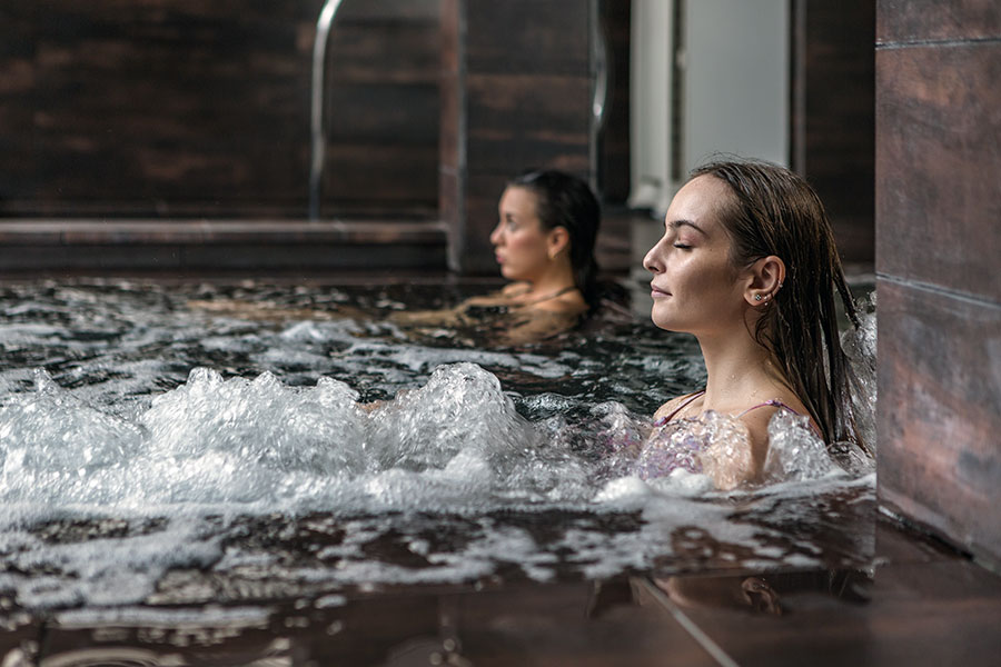 Two women sit in a pool with water jets and bubbles.