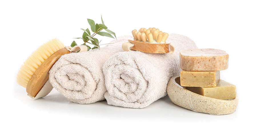 Two rolled, white towels sit next to a wooden brush and a pile of three bars of soap.
